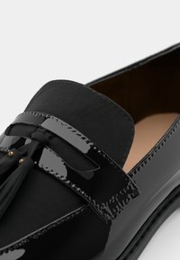Svarta lackläder loafers med en slät yta, platt design, dekorativ tofs och subtila sömnadsdetaljer.
