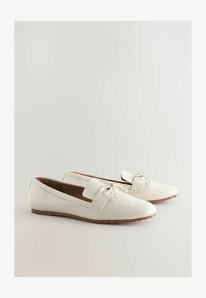Valkoinen patentsynteettinen nahkainen loafers-malli, jossa on pyöreä kärki, nauha-akcentti ja teksturoitu yksityiskohta sivussa. Litteä kumipohja, jossa on sileä pinta.