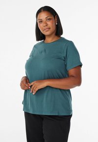 Teal kortärmad t-shirt med rund halsringning och tonalt logodetalj på bröstet, matchad med svarta byxor. Slätt bomullsmaterial.