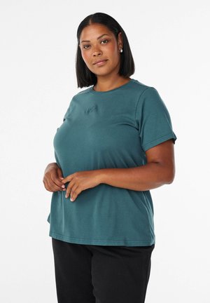 Türkises T-Shirt mit kurzen Ärmeln und rundem Halsausschnitt, versehen mit einem tonalen Logo-Detail auf der Brust, kombiniert mit schwarzen Hosen. Glattes Baumwollmaterial.