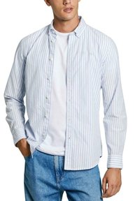Camisa de botones hecha de tejido ligero, con rayas verticales azules y blancas, un cuello puntiagudo y un corte holgado, usada sobre una camiseta blanca.