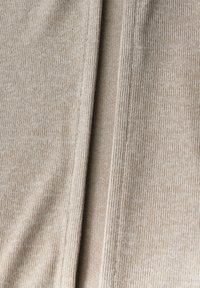 Beige ribbat tyg med en mjuk textur, som har vertikala linjer och subtila färgvariationer, prydligt vikt för att visa detaljer och struktur.