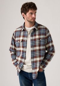 Rode, blauwe en crèmekleurige geruite flanellen shirt met een button-down kraag, twee borstzakken en lange mouwen, gelaagd over een witte henley.