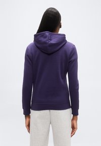 Μωβ φούτερ με απαλό ύφασμα, τσέπη καγκουρό και κουκούλα με κορδόνι. Διαθέτει μανίκια με μανσέτες και άνετη εφαρμογή.