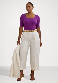 Top roxo de mangas curtas com nervuras, combinado com calças largas creme, realçado por um cinto tecido. Um blazer leve pendurado no braço.