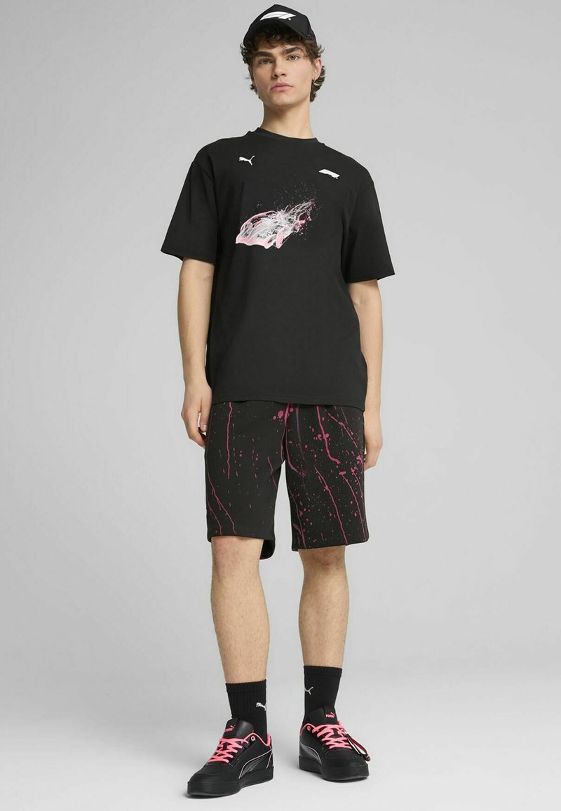 Sort T-shirt med pink grafik, mønstrede sorte shorts med pink sprøjt, sorte sneakers med pink snørebånd og en sort kasket.