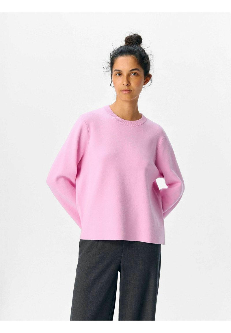 Maglione rosa a maniche lunghe con scollatura rotonda e vestibilità morbida, realizzato in un tessuto morbido e testurizzato. Abbinato a pantaloni scuri su misura.