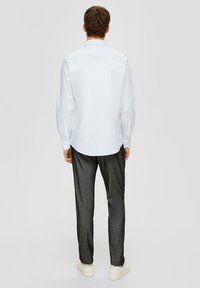 Camicia bianca a maniche lunghe con orlo curvo, abbinata a pantaloni grigio scuro a trama e scarpe bianche. Presenta polsini con bottone e colletto classico.
