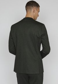 Dark green, tailored blazer with a smooth texture, structured shoulders, and a single vent at the back. Simple, minimal design.