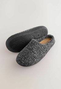 Grå uld slip-on slippers med tekstureret overflade og en sort gummisål med bølget mønster. Komfortabelt design til indendørs brug.