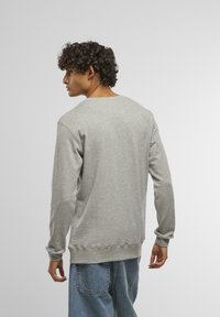 Sudadera gris de cuello redondo en algodón suave, con mangas largas y puños acanalados, combinada con jeans de mezclilla azul claro.