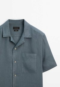 Chemise à manches courtes gris foncé avec boutons, poche poitrine et col replié, présentée sur fond blanc.