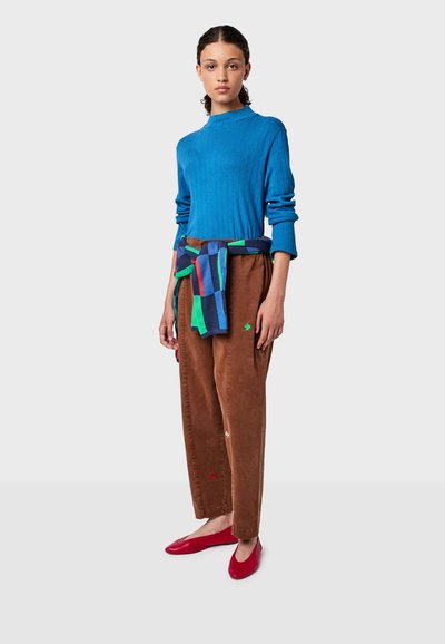 Maglione blu a coste con colletto alla coreana, pantaloni in velluto a coste marroni con dettagli sottili e ballerine rosse. Maglione a righe colorate legato in vita.
