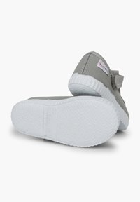 Scarpe di tela grigie con suole in gomma bianca, cinturino con chiusura a strappo e suola testurizzata. L'etichetta sul lato presenta un design multicolore.