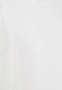 Top blanco de manga corta fabricado en un tejido suave y liso que presenta un diseño simple y clásico, con una textura sutil en la superficie.