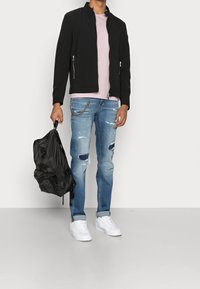 Veste noire légère, t-shirt rose pâle, jeans bleu clair déchirés, baskets blanches, tenant un sac à dos noir.