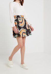 Vit blus med en nyckelhålsringning, parat med en svart kjol med ett färgglatt paisleymönster. Modellen bär ljusa slip-on skor.