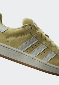 Zapatilla de ante amarilla con tres franjas grises, superficie texturizada, acentos en blanco y suela de goma. Presenta cierre con cordones y etiqueta "CAMPUS".