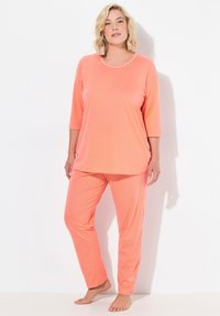 Korallfärgade pyjamaser med en löst sittande topp med rund halsringning och 3/4-ärmar, tillsammans med byxor med elastisk midja i prickigt mönster.