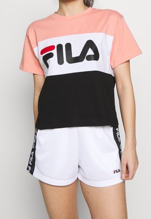 Roze, wit en zwart kleurig crop top met "FILA" logo; gecombineerd met witte shorts met zwarte zijaccenten en logo.