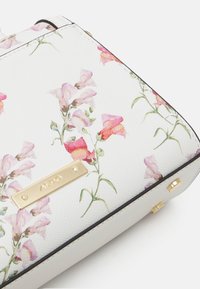 Torebka na ramię o białej fakturowanej powierzchni z różowymi i pomarańczowymi wzorami kwiatowymi. Złote akcenty i logo na przedzie.