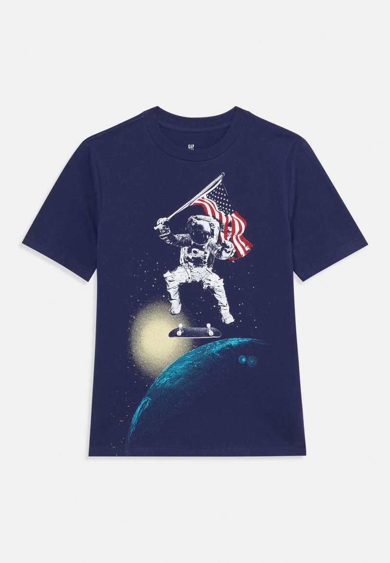 Navy zila kokvilnas T-kreklu, kurā attēlots astronoms, kas brauc ar plati un tur Amerikas karogu, fona ir stilizēta planēta un zvaigznes.