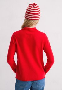 Czerwona, długosleeve sweter z okrągłym dekoltem, połączony z czerwono-białym czapką w paski. Miękka tekstura, luźny krój i widoczne szwy.