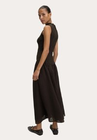 Bruine, mouwloze jurk met een gestructureerde lijfje en een vloeiende, patroonrokken. Draag met zwarte flats, wat een aansluitende silhouet toont.