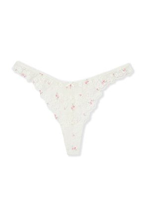 Tanga en dentelle blanche avec de petits accents floraux roses et des bords festonnés, présenté à plat sur un fond blanc.