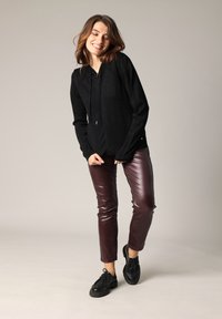 Zwarte hoodie met lange mouwen en koord, gecombineerd met bordeauxglanzende slim-fit broek en zwart veterschoenen. Effen achtergrond.
