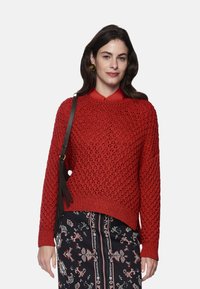 Red knitted sweater with a textured pattern, round neckline, and ribbed cuffs. Paired with a black patterned skirt featuring floral designs.