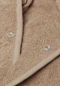 Tissu de couleur tan avec une finition douce, comportant des fermetures à pression en argent et un bord lisse beige le long des bords.