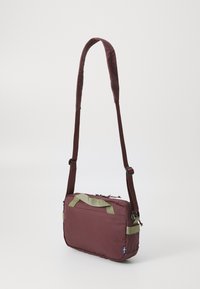 Borsa a spalla color bordeaux con dettagli verde, tracolla imbottita, forma rettangolare, doppi manici superiori e chiusura con zip. Presenta un piccolo dettaglio con logo.