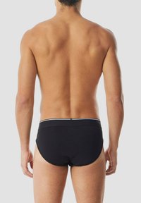 Schwarze Badehose mit weißem elastischem Bund, enganliegendem Schnitt und glatter Textur, von hinten an einer Person gezeigt.