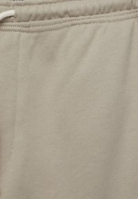 Beige sweatpants feature a soft cotton blend, elastic waistband, and stitched seams, with a smooth texture and no visible patterns.