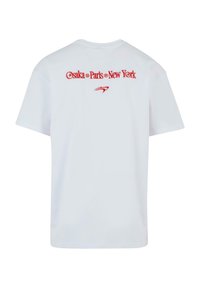 White t-shirt featuring bold red text on the back: "Osaka • Paris • New York" with an accent graphic below. Plain, short-sleeved design.