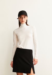 Witte lange mouwen turtleneck top gecombineerd met een zwarte rok met een zij-split. De pet is zwart met een verhoogd logo.