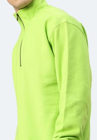 Helles limonengrünes Fleece mit Reißverschluss und hohem Kragen, mit einem Frontreißverschluss und glatter Textur. Stilvolle Nähte entlang der Seiten und Schultern.