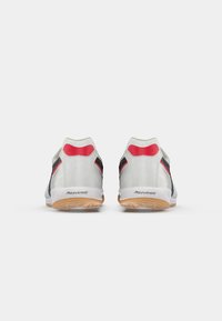 Witte sport schoenen met rode en zwarte accenten, glad synthetisch materiaal, laag ontwerp, en een gestructureerde gumrubber zool.
