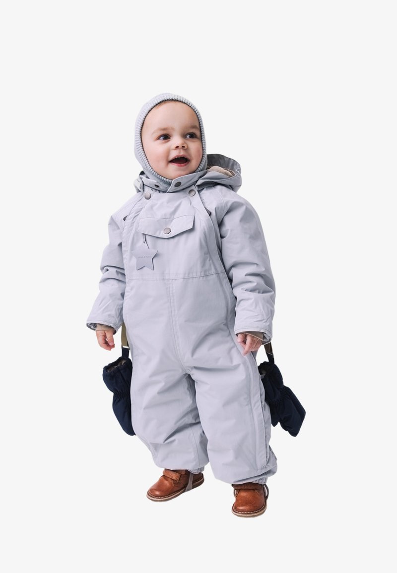Svetlo šedý jednodielny snowsuit s zipsom, odnímateľnou kapucňou a detailom hviezdy. Nosí sa s hnedými bootami a tmavomodrými rukavicami, stojaci postoj.