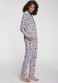 Kvetinový pyžamový set s modrým pozadím a ružovými a bielymi kvetmi, dlhými rukávmi, vreckami a voľnými nohavicami. Mäkká textúra látky.