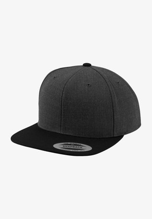 Casquette snapback grise en tissu texturé avec une visière plate. La casquette est ornée d'une étiquette circulaire à l'avant et est associée à un t-shirt noir uni.