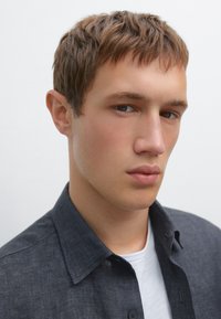 Dark gray shirt with a collar, worn over a white T-shirt. The fabric appears textured with a subtle weave. Features a buttoned front.