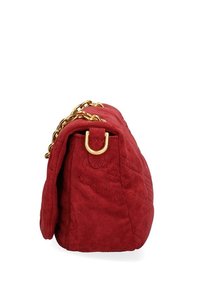 Sac à main en suède rouge avec un design matelassé, une bandoulière en chaîne dorée et des accessoires en métal. Il présente une forme structurée et une fermeture à rabat.