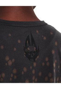 Camiseta negra con manchas de lejía, cuello redondo, con un gráfico central de calavera y adornos decorativos en la parte de atrás. Textura de algodón suave.