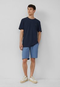 Marineblauwe katoenen T-shirt, korte mouwen, ronde halslijn, gecombineerd met lichtblauwe shorts. Witte sneakers met tan accenten maken de outfit compleet.