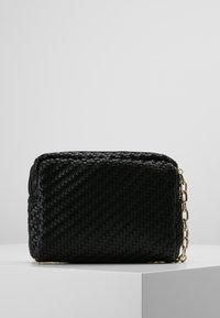 Sac tissé noir avec une forme rectangulaire, surface texturée et accent en chaîne dorée. Design compact avec une fermeture zippée.