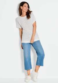 Lichtgrijs gebreid topje met korte mouwen, voorzien van een textuurpatroon, gecombineerd met cropped blauwe spijkerbroek en witte sneakers.