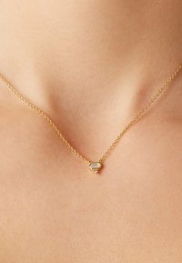Gouden ketting met een hexagonaal hanger met een doorzichtig middenstuk en een kleine strassaccent, rustend tegen de huid.