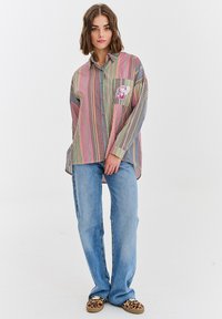Koszula w paski w wielu kolorach z zapięciem na guziki i kieszonką na piersi. Posiada różowe guziki oraz luźny krój. Połączona z jasnoniebieskimi dżinsami.
